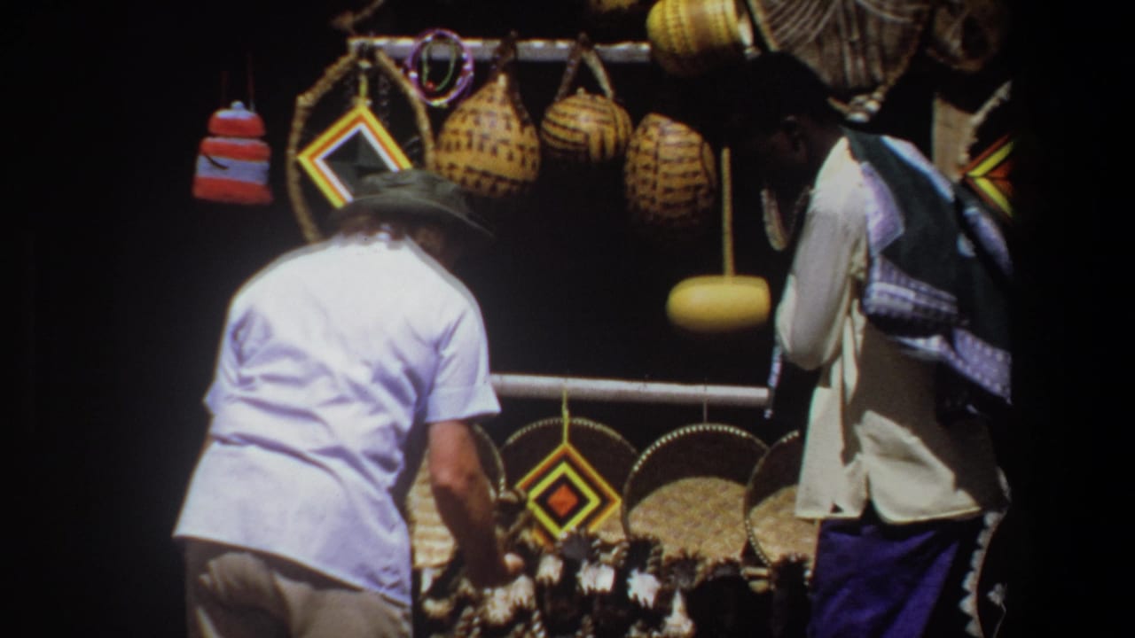 In Pretoria, South Africa in 1969, a white-hatted man browses woven baskets and geometric craft items at a shaded outdoor stall.