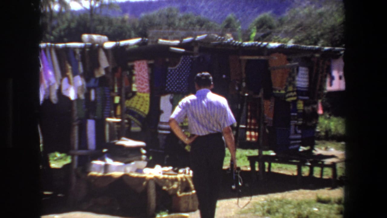 Man stands closer to a fabric stall with textiles hanging across the front.