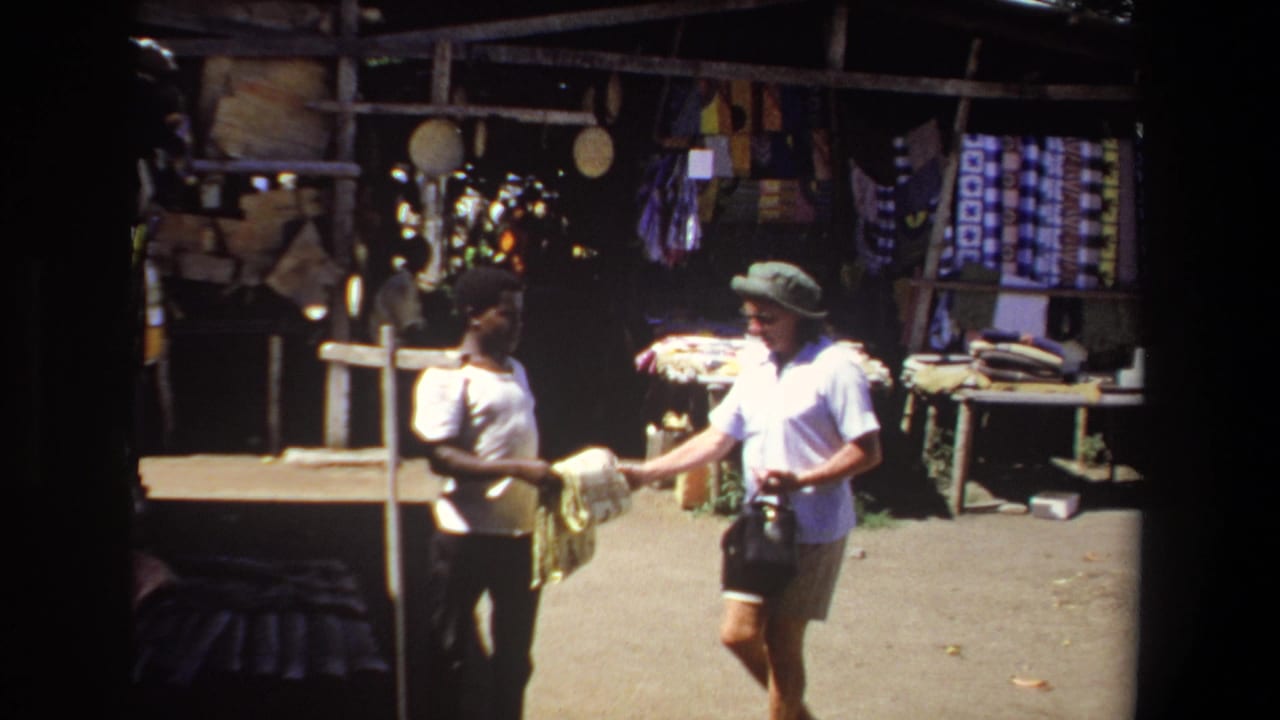 A woman in a sun hat receives or examines a patterned rug beside a vendor at an outdoor stall.