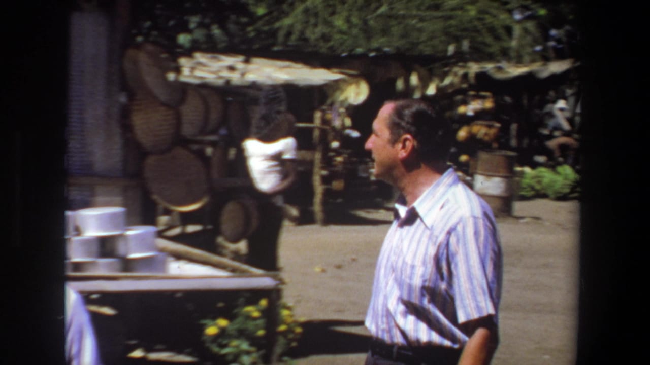 1969 Pretoria market scene with a striped-shirt traveler passing shaded stalls, woven baskets, tables, and containers.