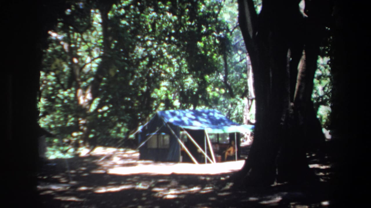 1969 Pretoria home-movie frame showing a blue canvas tent beneath large trees in dappled shade.
