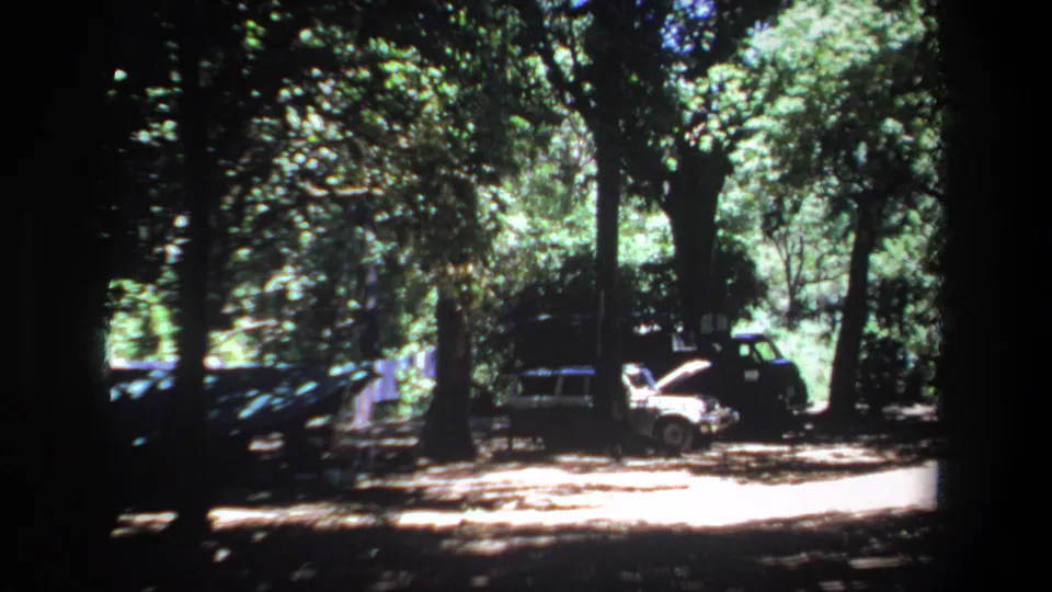Pretoria 1969 8mm frame showing a shaded roadside or parking area with older cars clustered beneath trees.