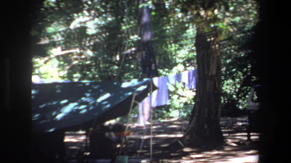 A shaded 1969 Pretoria campsite detail shows a dark tarp or tent, laundry on a clothesline, tree trunks, and bright foliage beyond.