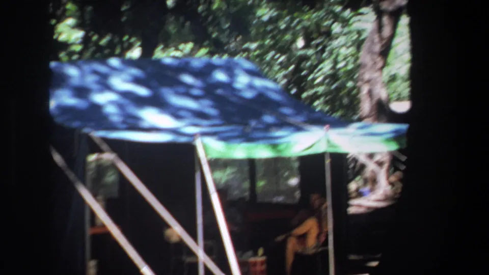 Pretoria 1969 home-movie frame of a canopy tent among trees, with seated people visible in the shaded interior.
