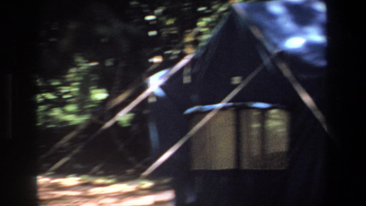1969 Pretoria home-movie frame showing a dark canvas camp shelter with poles, a small table, and forest light outside.