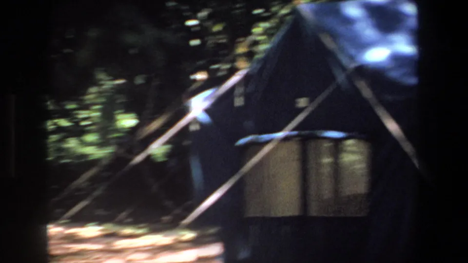 1969 Pretoria home-movie frame showing a dark canvas camp shelter with poles, a small table, and forest light outside.