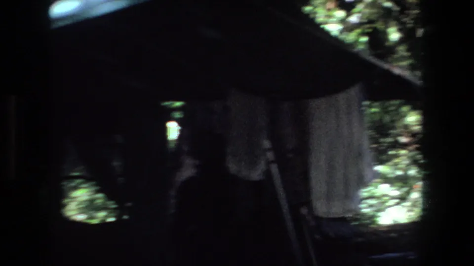 Dim 8mm frame from the Pretoria campsite, with hanging fabric and tent supports silhouetted against forest openings.
