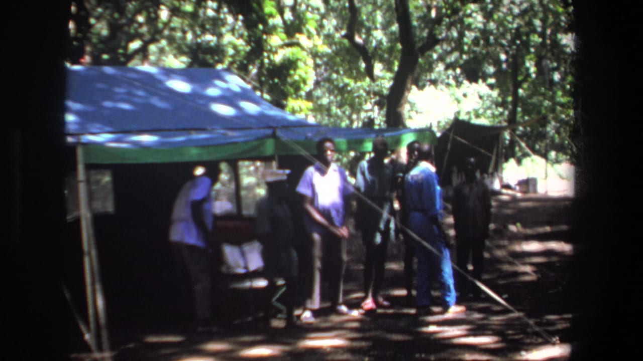 1969 Pretoria home-movie frame showing several men near a blue and green tent under trees in dappled sunlight.