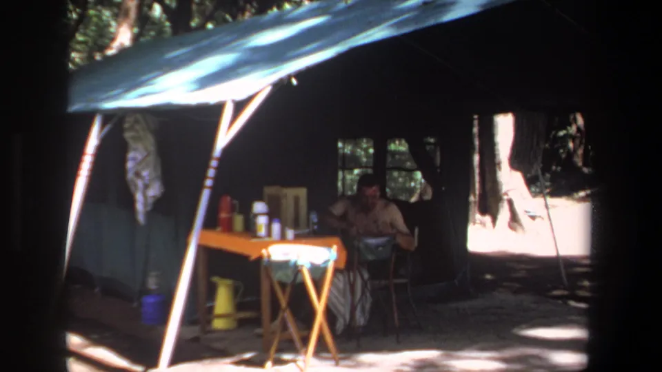 A 1969 Pretoria campsite view shows the man seated deeper in the tent, with the table and containers catching bright sun at the entrance.