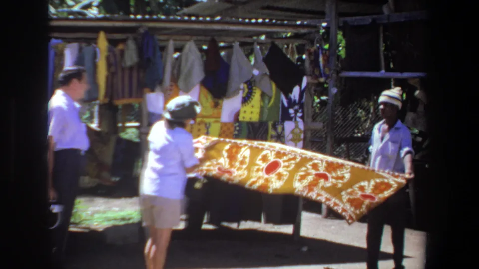 At the Pretoria outdoor market, the woman appears to inspect the yellow patterned cloth while the vendor keeps it stretched open.