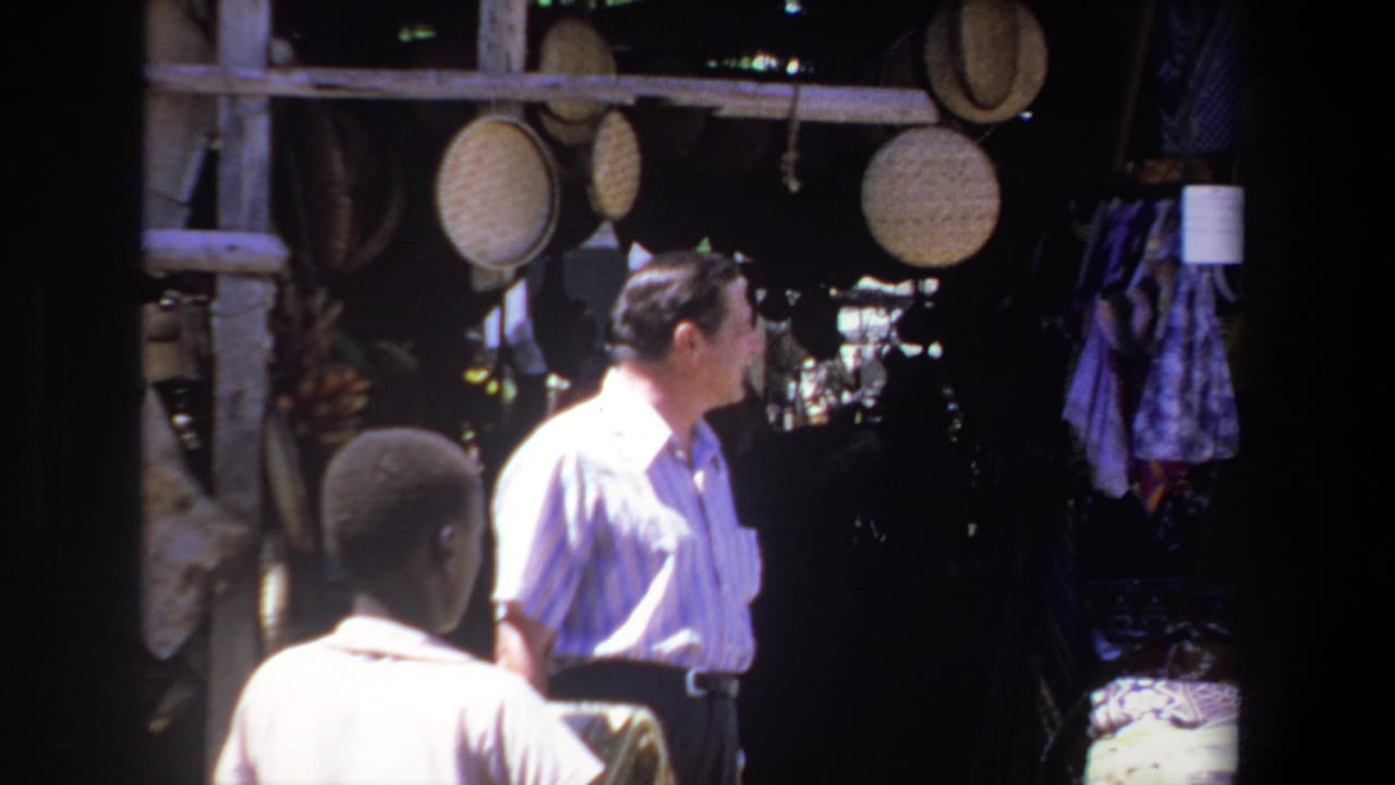 A man stands beside a market stall with woven baskets hanging above him.