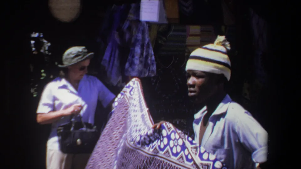 A woman with a handbag and a vendor in a striped cap stand by a patterned textile in Pretoria, South Africa, 1969.