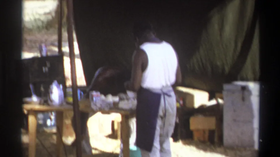 A man in a white tank top and dark apron stands at an outdoor prep table in Cape Town, South Africa, 1969.