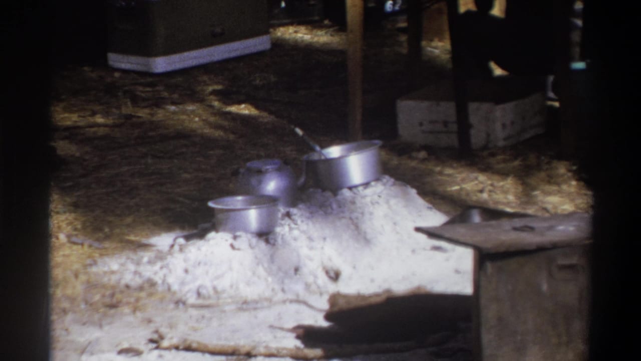 Metal pots and pans sit on a white mound beside wooden boxes under a shelter.