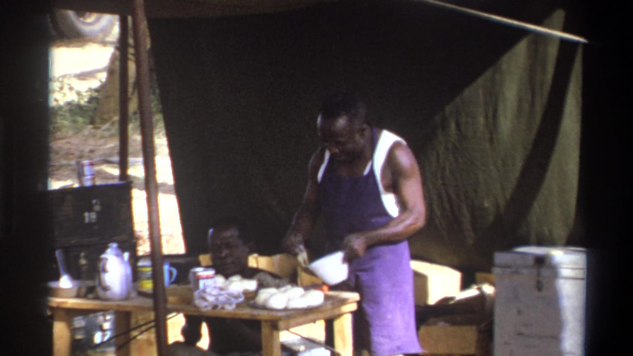 Cape Town, South Africa, 1969 home-movie frame showing one man in an apron preparing food while another sits beside a table under a tent.