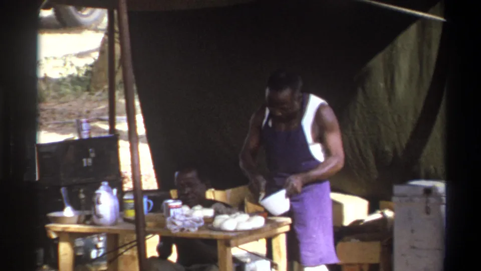 Cape Town, South Africa, 1969 frame showing food preparation under a tent with a seated man partly visible behind the table.