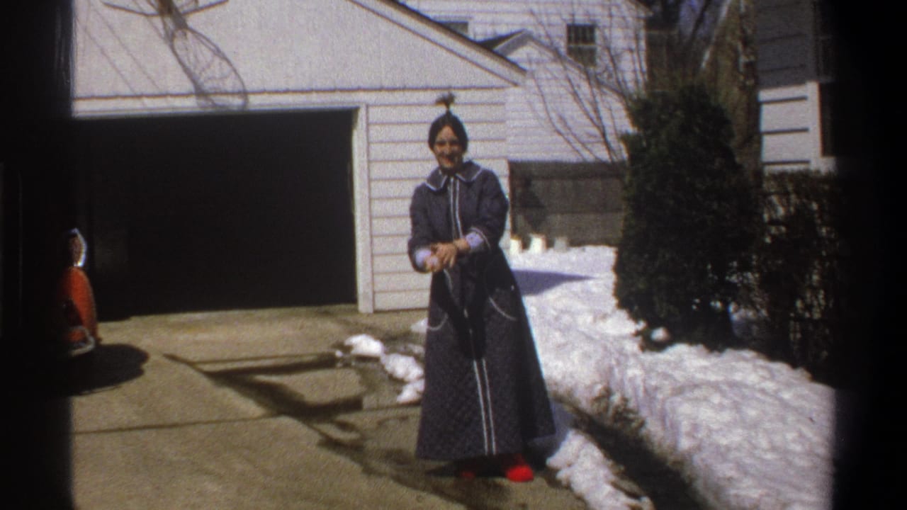 1969 Cape Town frame of a woman in a blue robe facing the camera in a residential driveway bordered by snow.