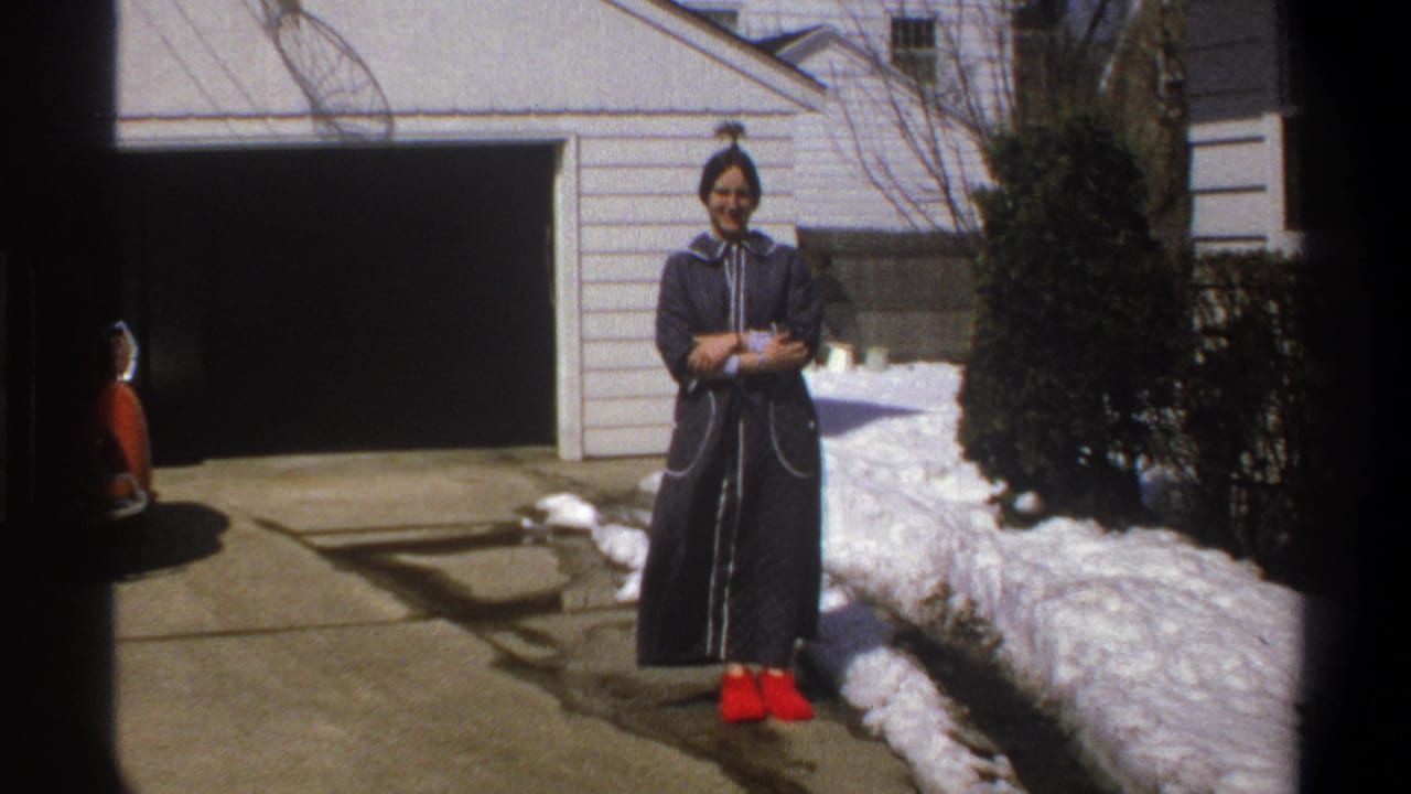 Young woman smiling in a dark robe and red shoes near snow and a garage.