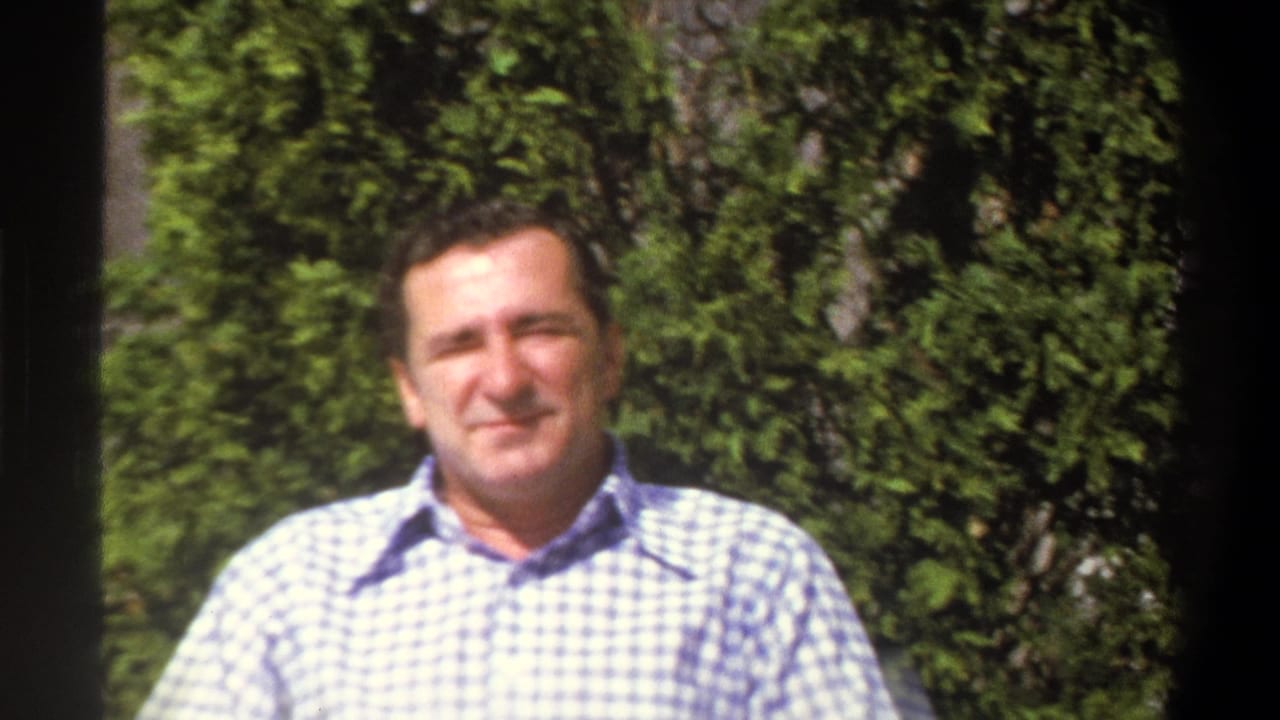 Adult man seated outside, framed closely against green foliage.