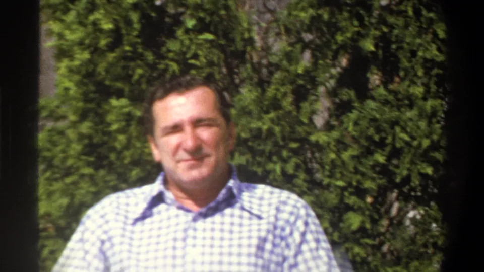 The adult man remains seated outdoors in the Cape Town garden setting, softly focused against dense green foliage.