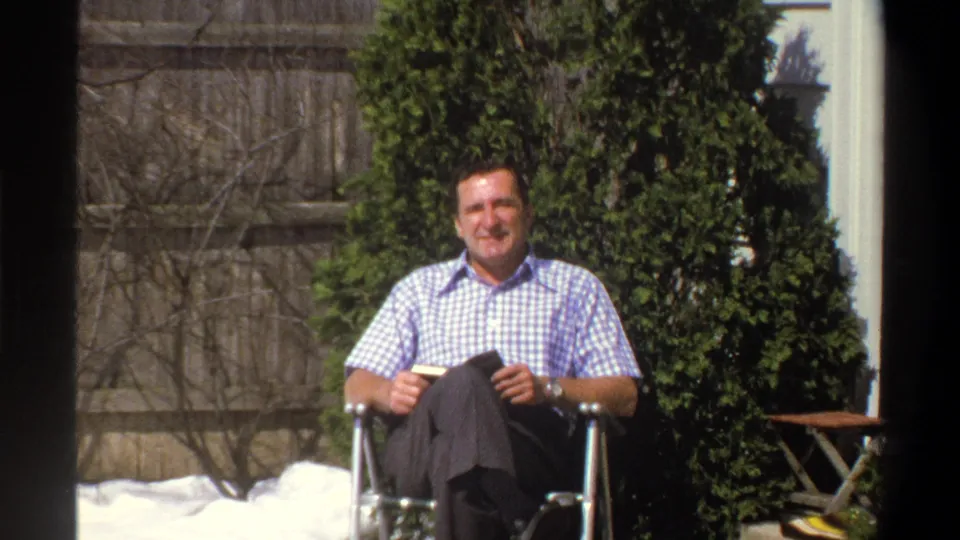 A wider garden view shows the adult man seated in a metal lawn chair in 1969 Cape Town, with hedge, fence, and yard details visible.