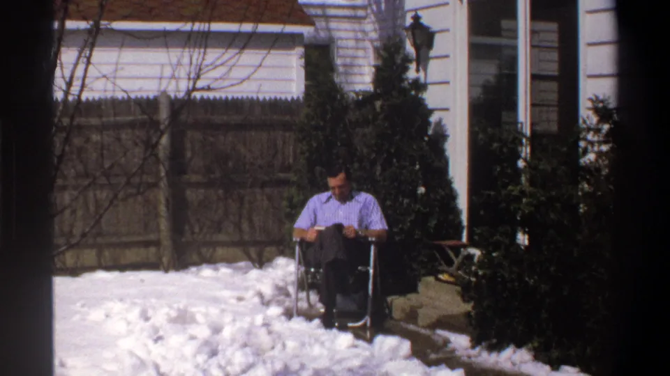 The final frame shows the man still seated in the wheelchair, reading in a snow-covered residential yard with fence and shrubs behind him.