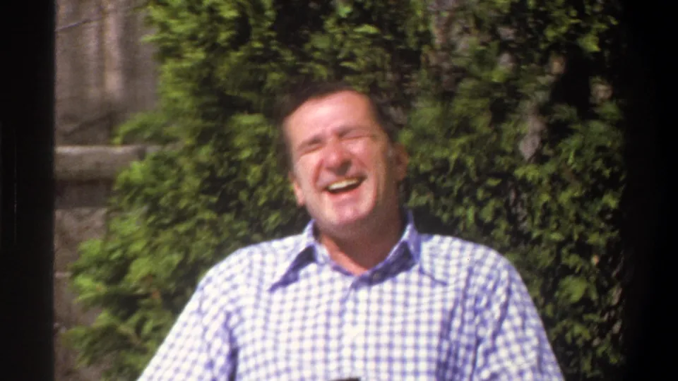 The seated man laughs heartily with his head tipped back, framed by foliage in the Cape Town 1969 8mm footage.