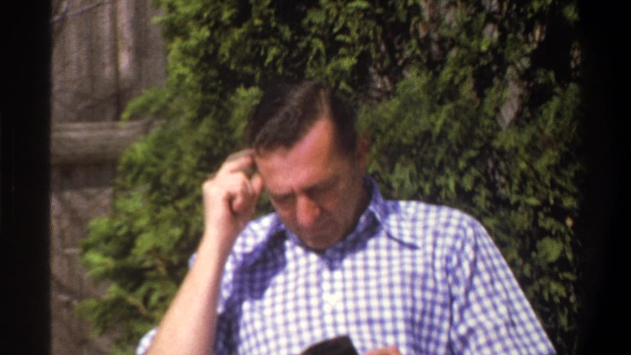Man seated outdoors looks down with one hand near his head and a book in his lap.