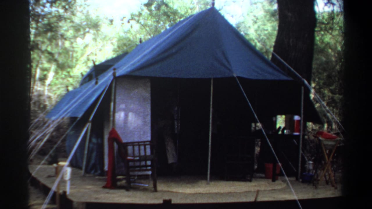 1969 Khartoum, Sudan home-movie frame showing a blue canvas tent among trees, with camp furniture near the entrance.