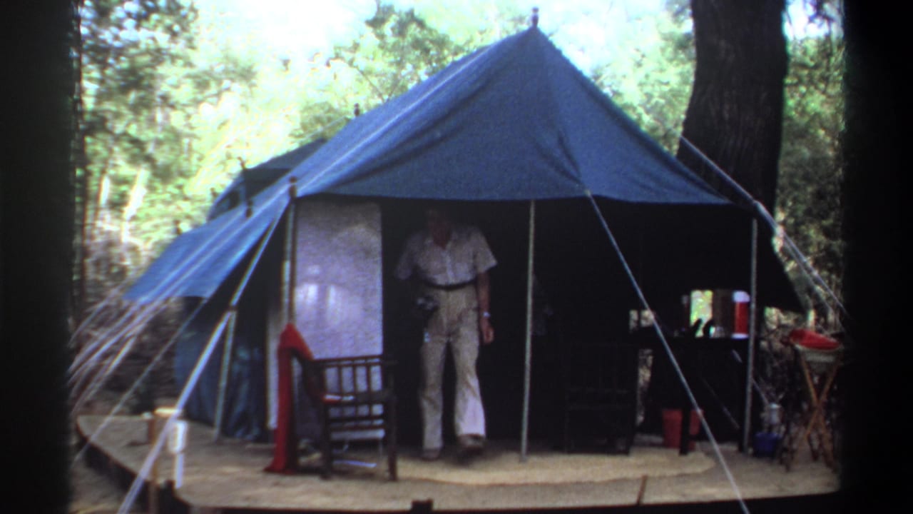 Adult man appears in the entrance of a blue canvas tent at a wooded camp identified as Khartoum, Sudan, 1969.