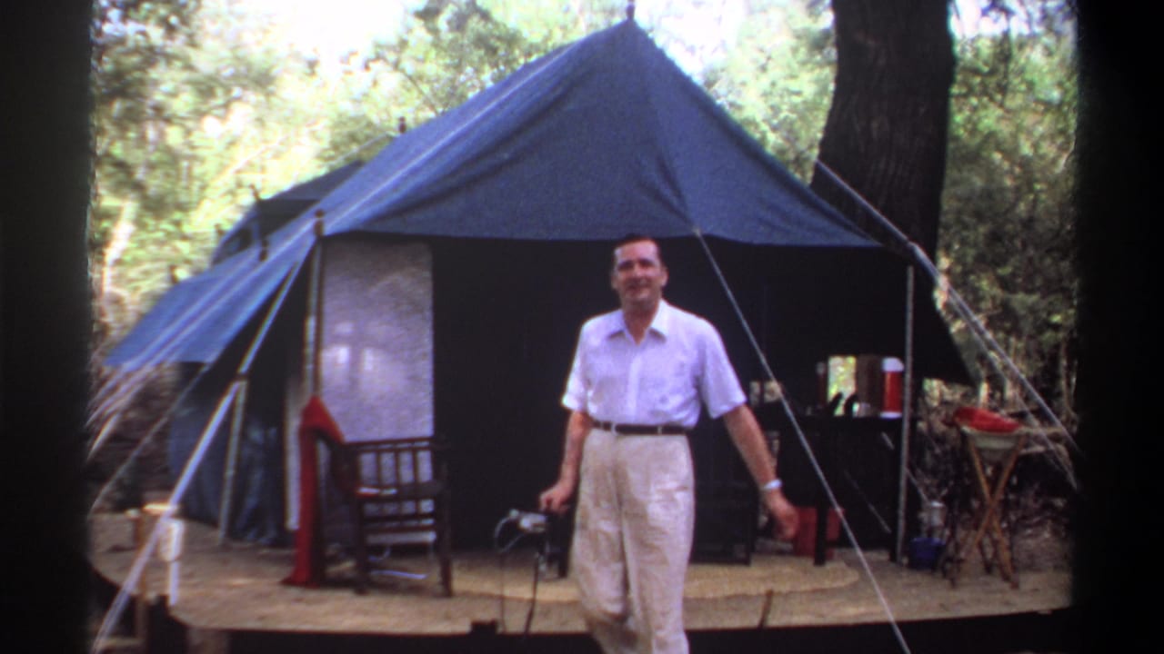 Man walking from the front of a blue tent while holding a small object.