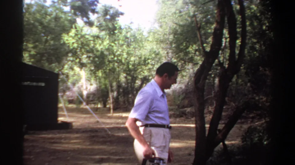In 1969 Khartoum home-movie footage, a man in khaki trousers walks beneath trees with a camera in hand.