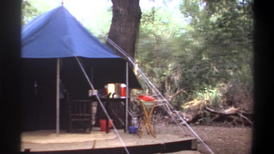 1969 Khartoum home-movie view of a blue campsite tent with furniture and supplies arranged outside.