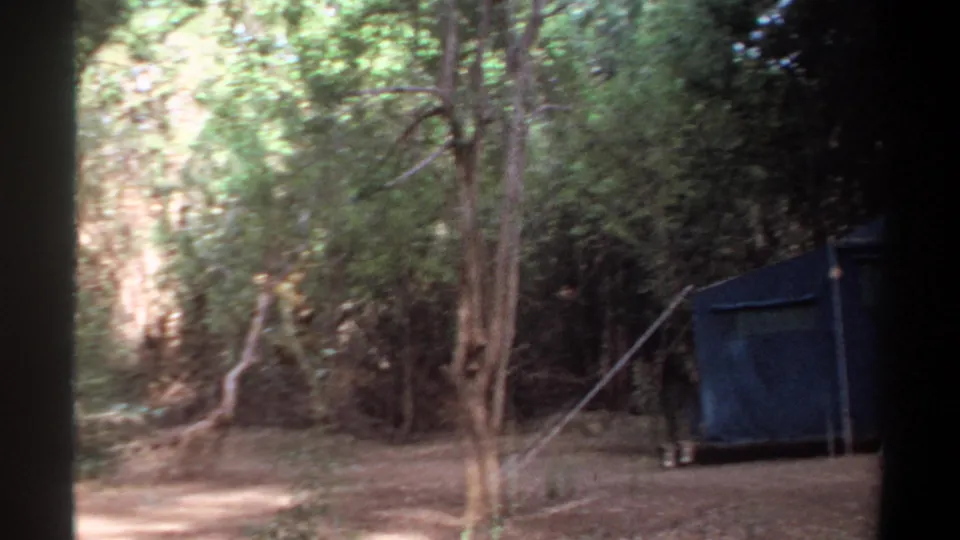 1969 Khartoum home-movie frame showing the blue canvas tent partly in view beside trees and a dry forest clearing.