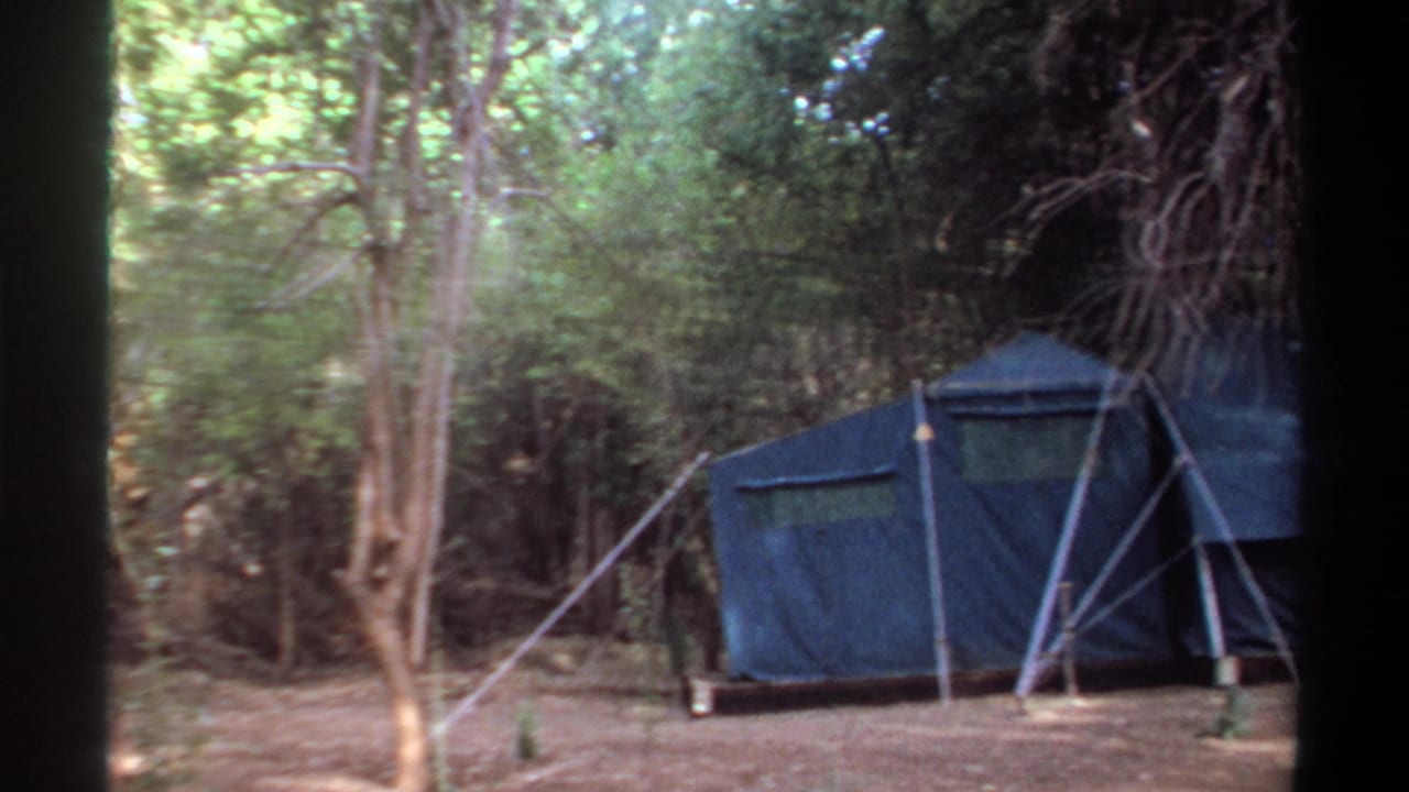 1969 Khartoum home-movie frame showing a blue canvas tent set among trees in a dirt clearing.