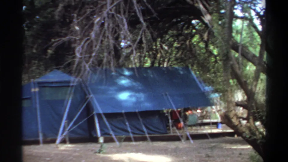 1969 8mm frame from Khartoum showing the side of a blue canvas tent and shaded campsite objects.