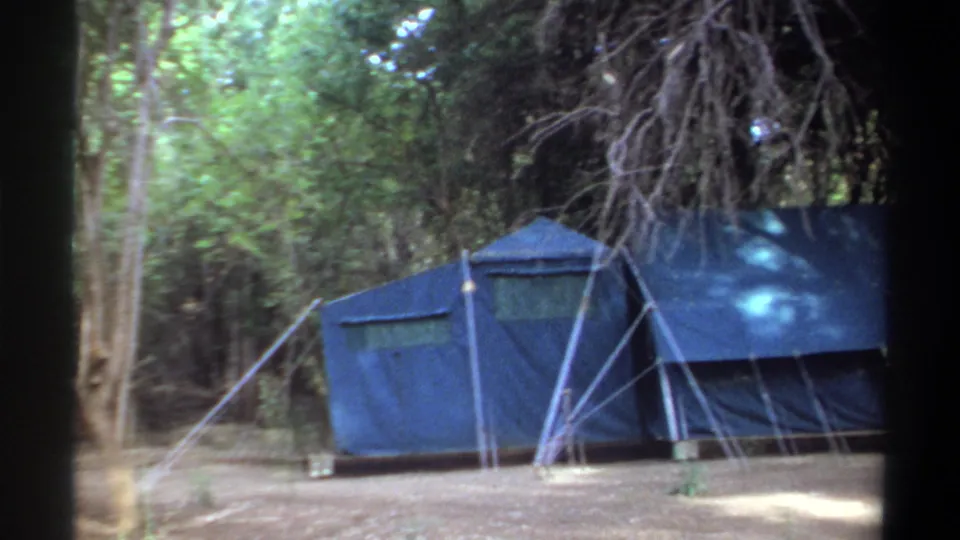 Khartoum 1969 home-movie view of a blue tent framed by trees, ropes, and soft forest light.
