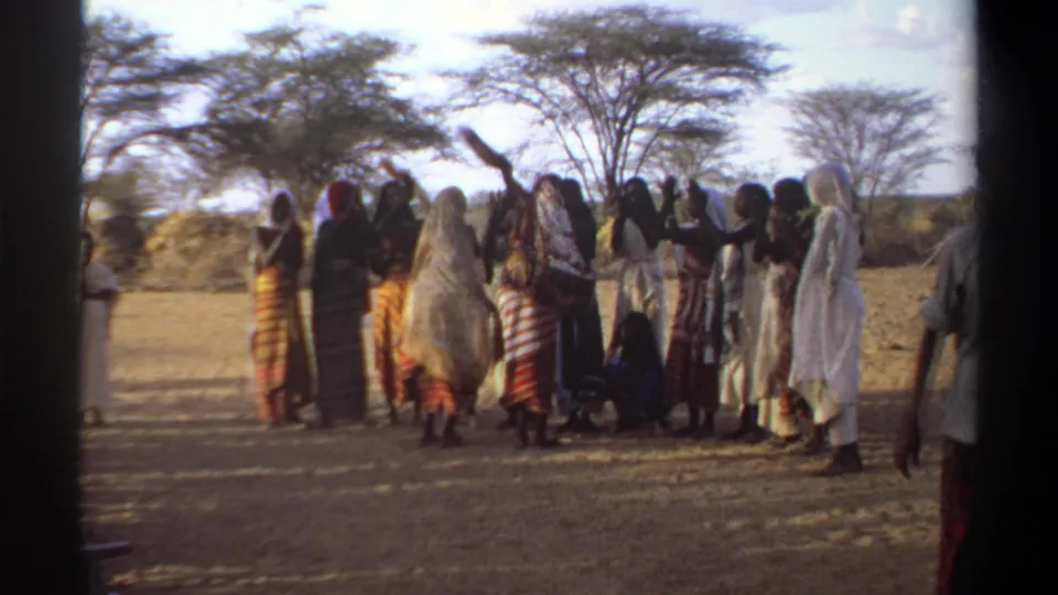 1969 Khartoum frame showing the outdoor group in motion, with raised arms and a figure entering from the right edge.