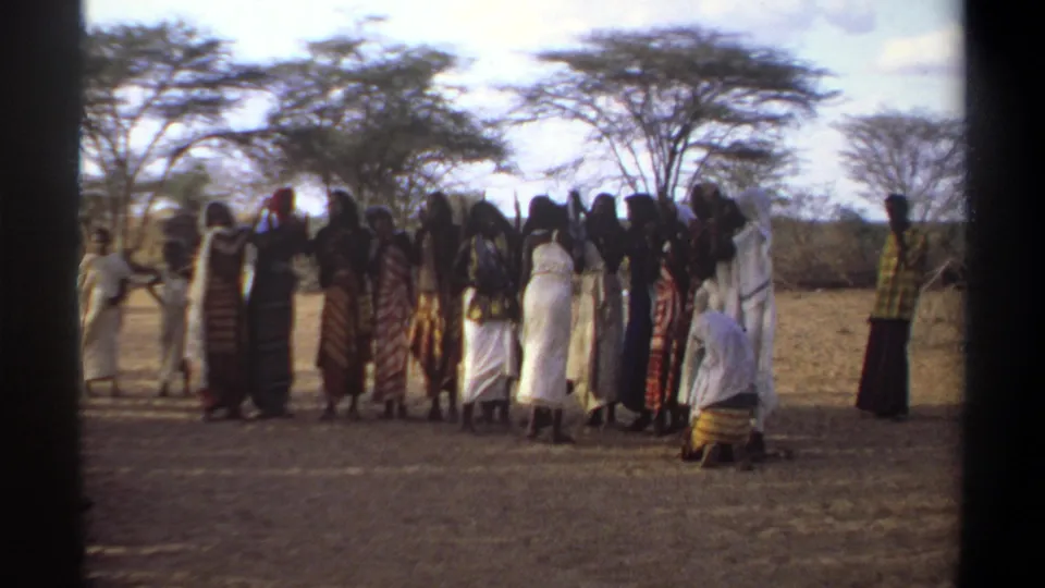 1969 Khartoum home-movie frame showing women in patterned and white garments gathered outdoors beneath sparse trees.