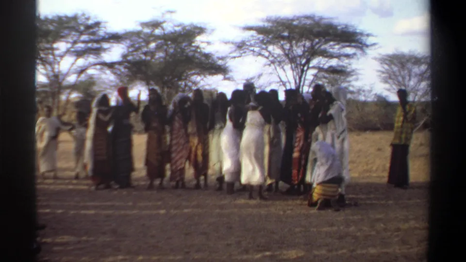 1969 Khartoum frame with women in colorful wraps and white clothing gathered in an open dry area near trees.