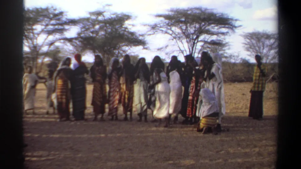 1969 Khartoum home-movie still of women in traditional dress standing closely together in a sunlit dry landscape.