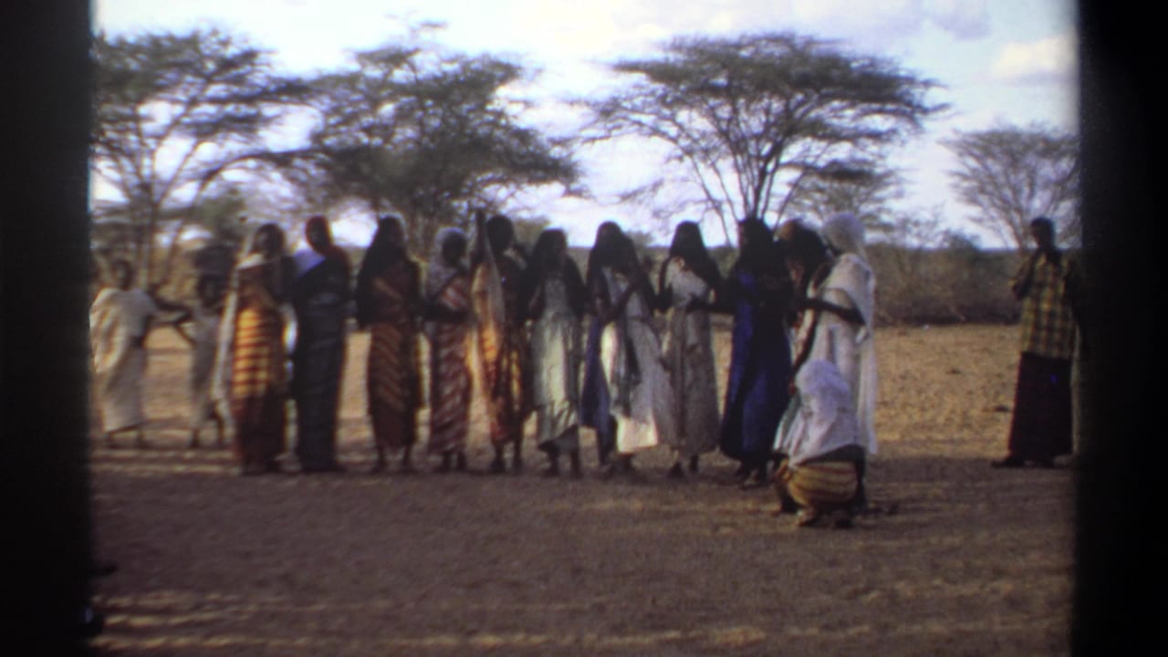 In 1969 Khartoum footage, women and girls in flowing robes and headscarves clap together on dry ground under trees.