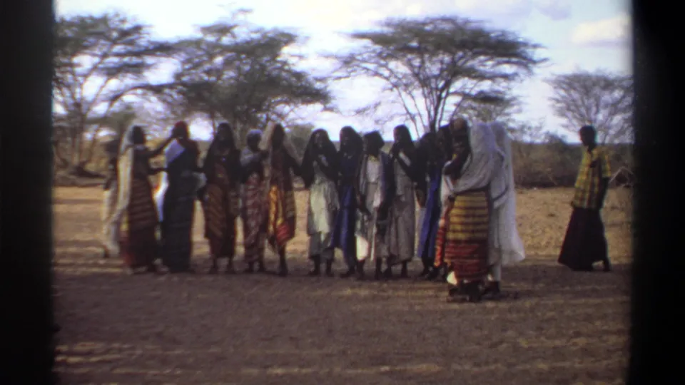 The 1969 Sudan frame shows women and girls in pale and patterned robes clapping together on a dusty outdoor path.