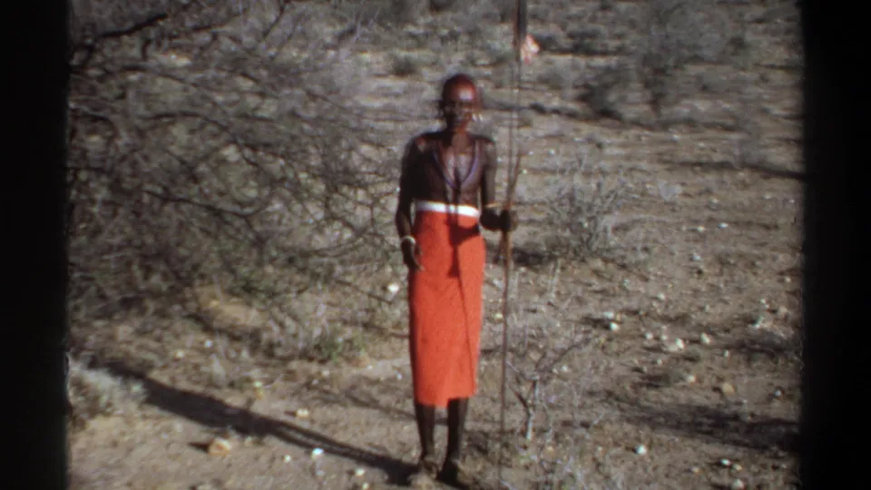 1969 Khartoum, Sudan 8mm frame of a man in an orange wrap standing near thorny brush with a spear.