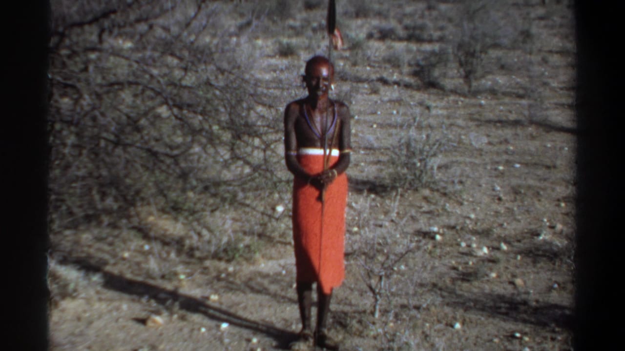 Man facing the camera with a staff, framed against dry ground and brush.