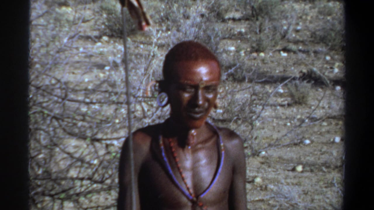 1969 Khartoum home-movie frame showing a carved human figure near a dry path and sparse vegetation.