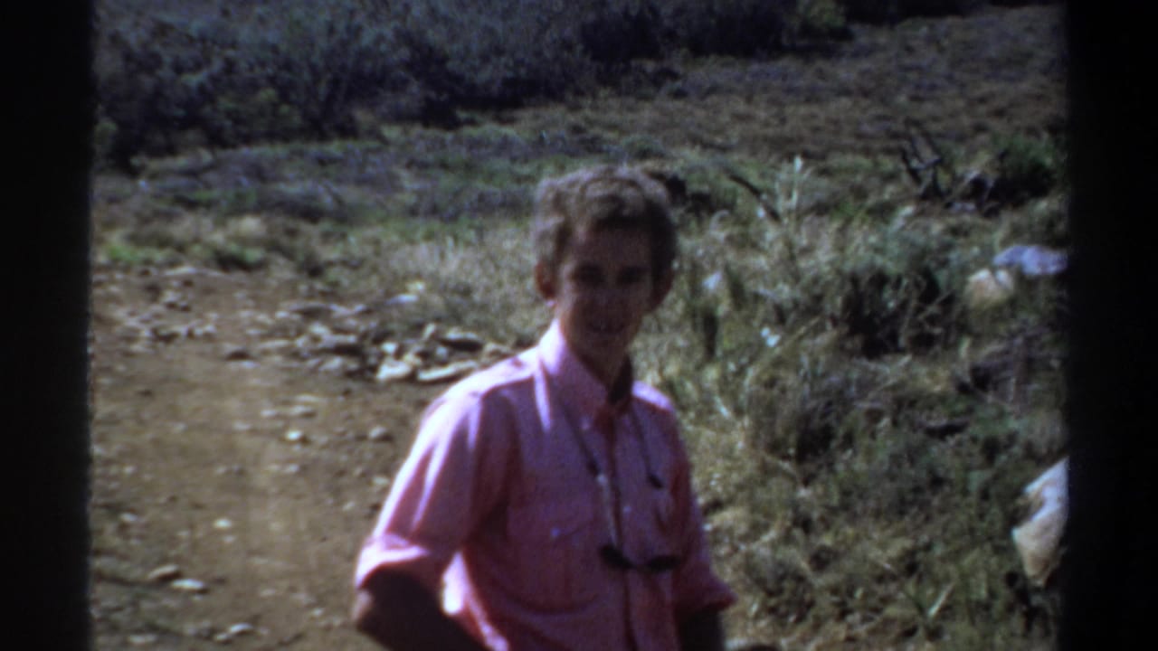 1969 Khartoum frame with a man in a pink shirt walking toward the camera on a dry dirt path.