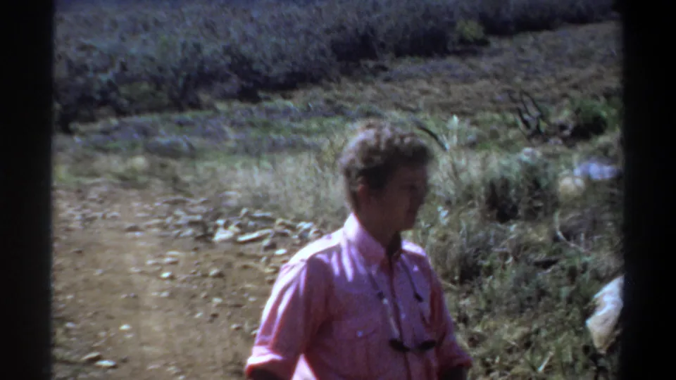 1969 Khartoum home-movie frame showing the man in profile as he walks past scrub and rocks.