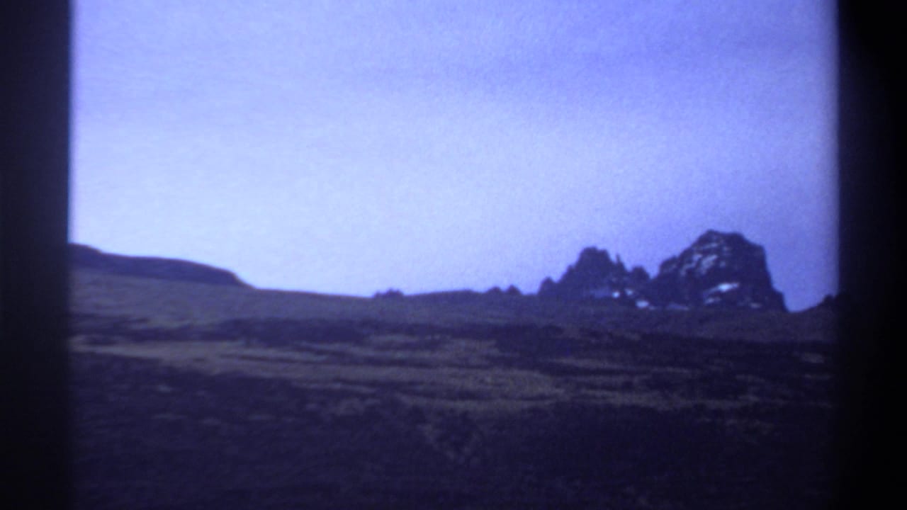 A wide 1969 Sudan landscape view shows a distant rocky outcrop across dark arid ground beneath a blue sky.