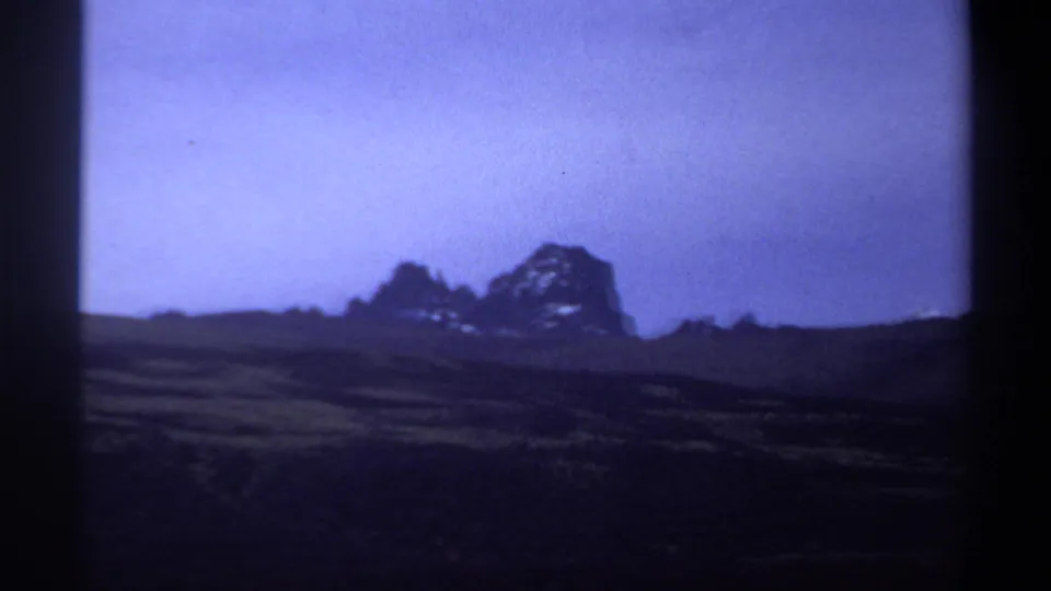 The 8mm frame shows a distant rock formation rising above arid Sudan terrain, with strong blue color shift.